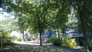 Un chemin menant à un bâtiment doté d’un toit en pente, entouré d’arbres et d’une zone herbeuse.