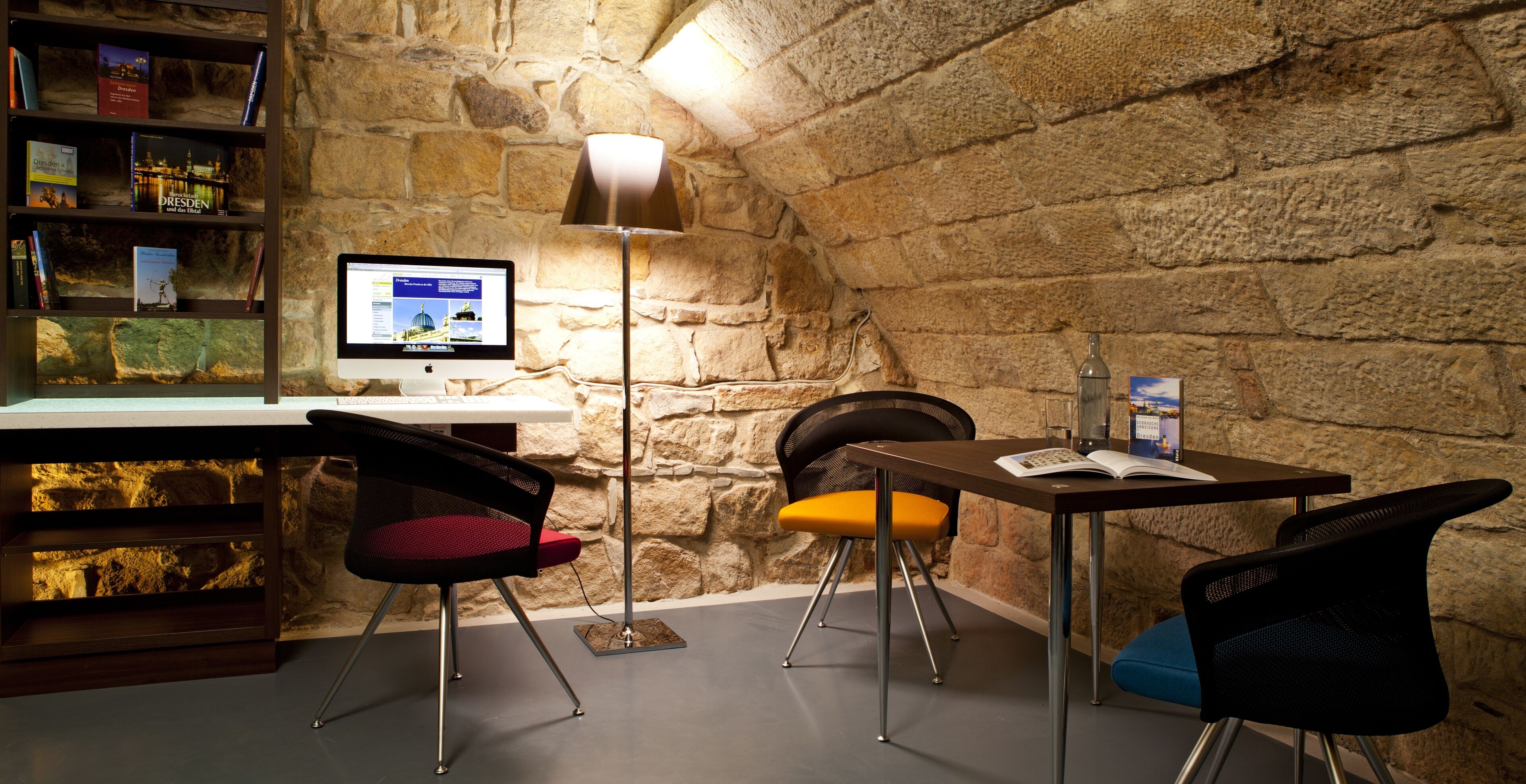 Eine gemütliche Leseecke mit einer Steinwand, einem Schreibtisch, einem Computer und zwei Stühlen.