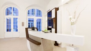A reception area with a curved white reception desk, a large arched window, and a vase with dried plants. - Hapimag Resort Dresden (Dresden)