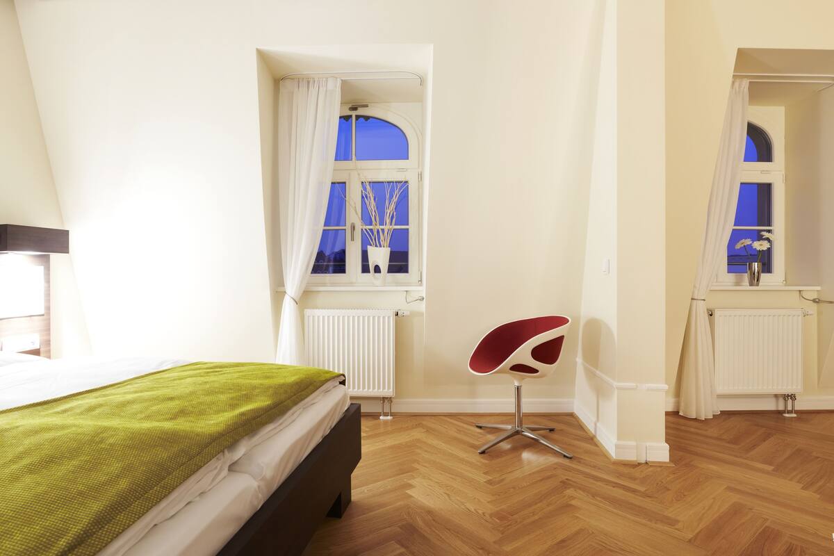 A bedroom with a bed, a chair, a window, and a radiator.