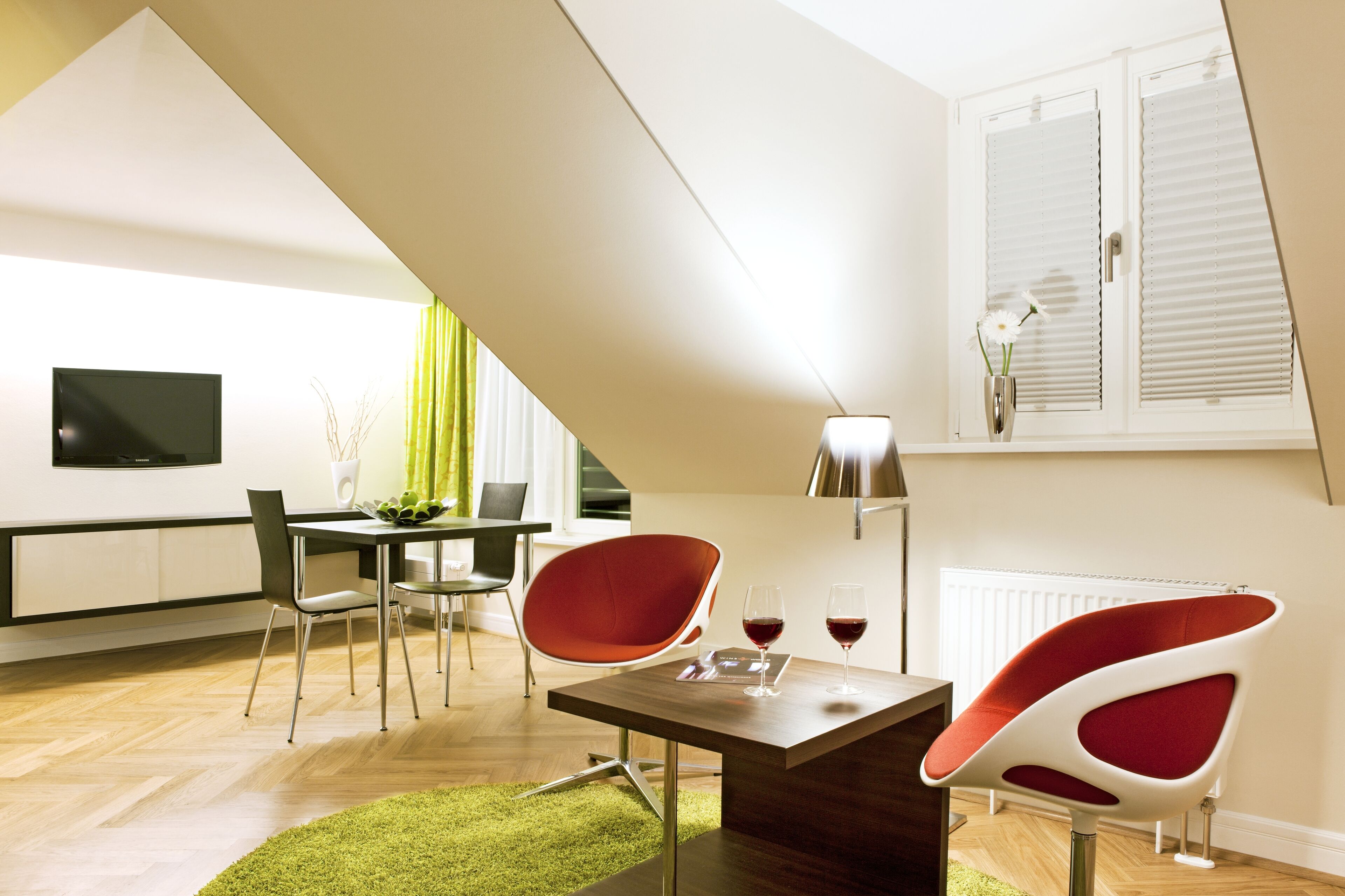 Un salon moderne comprenant un coin repas, un téléviseur fixé au mur et une fenêtre avec des stores.