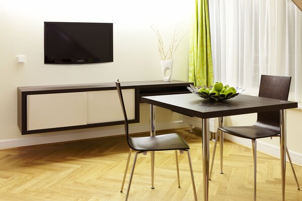 A modern dining area with a flat-screen TV mounted on the wall, a table with chairs, and a vase with branches on the side. - Hapimag Resort Dresden (Dresden)