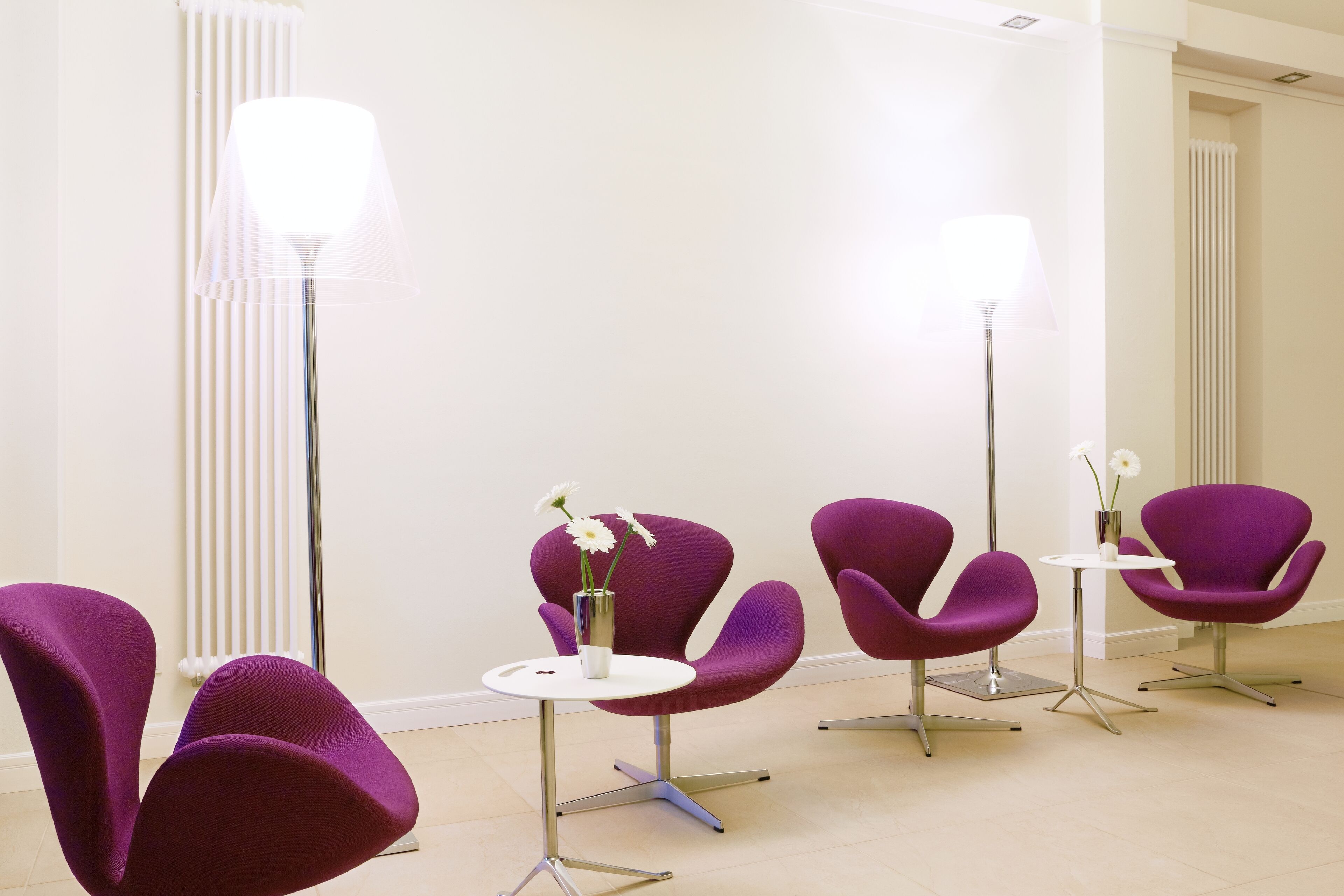 Ein moderner Wartebereich mit violetten Stühlen, weißen Tischen und einer hohen Stehlampe.