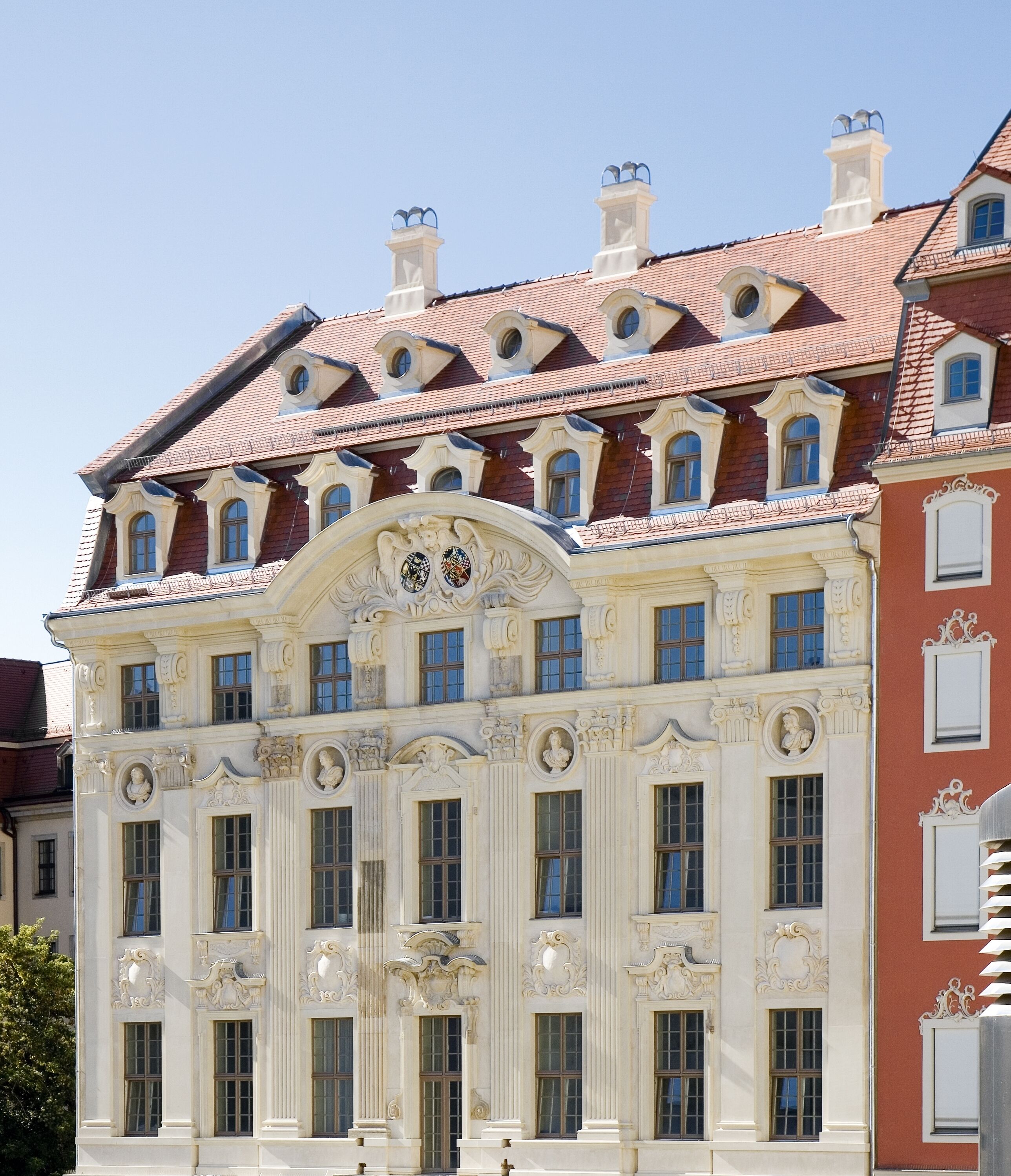 Een historisch pand met klassieke architectuur, met versierde gevels, meerdere ramen en een dak van rode tegels.