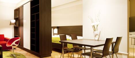 Una habitación de hotel moderna con zona de comedor, una cama con cubrecama verde y un armario grande.