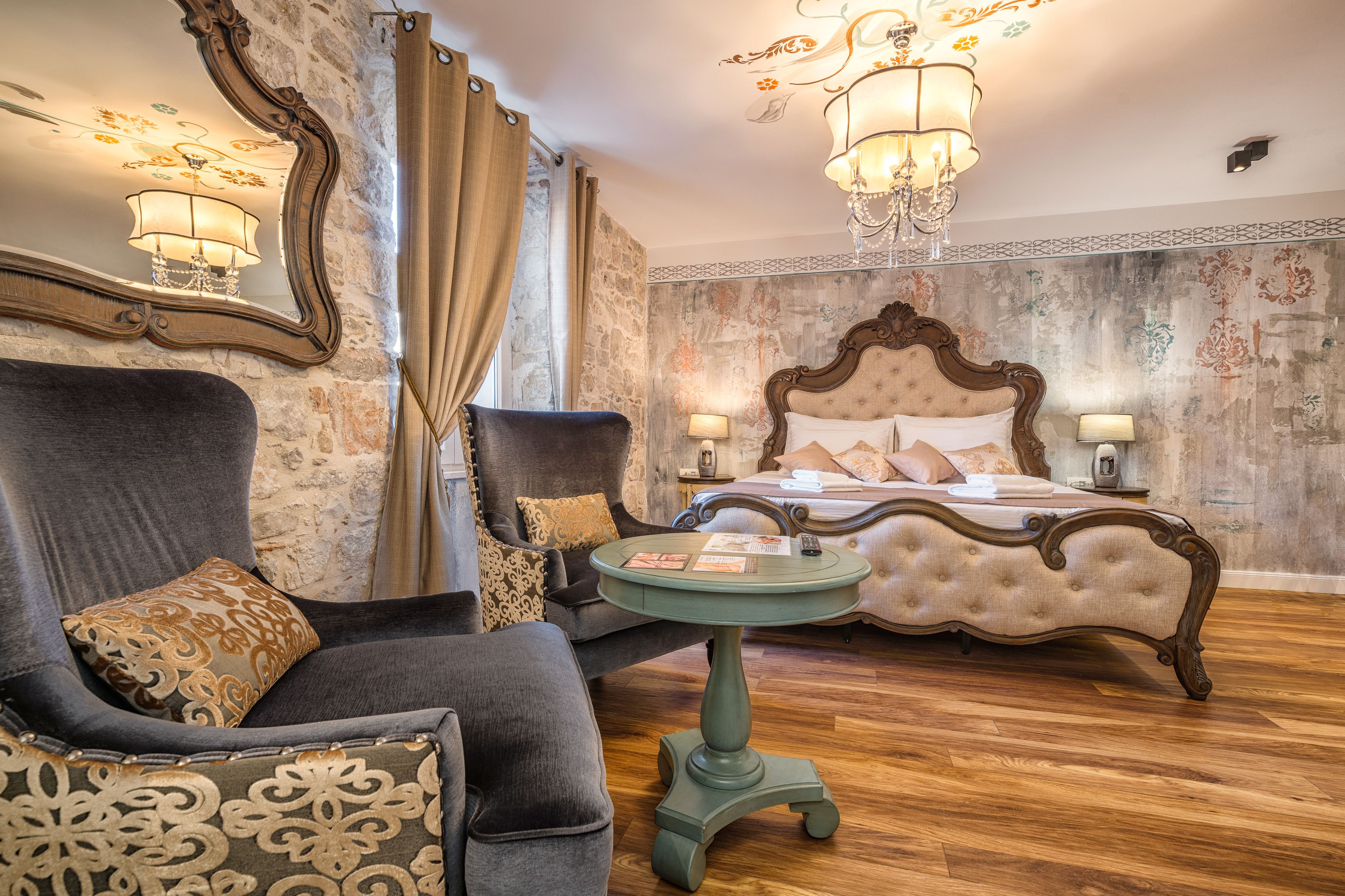 Ein Hotelzimmer mit einem großen Bett, einer Sitzecke mit Stuhl und Tisch sowie einem dekorativen Spiegel.