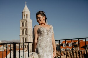 A person in a wedding dress standing on a balcony with a historic tower in the background.