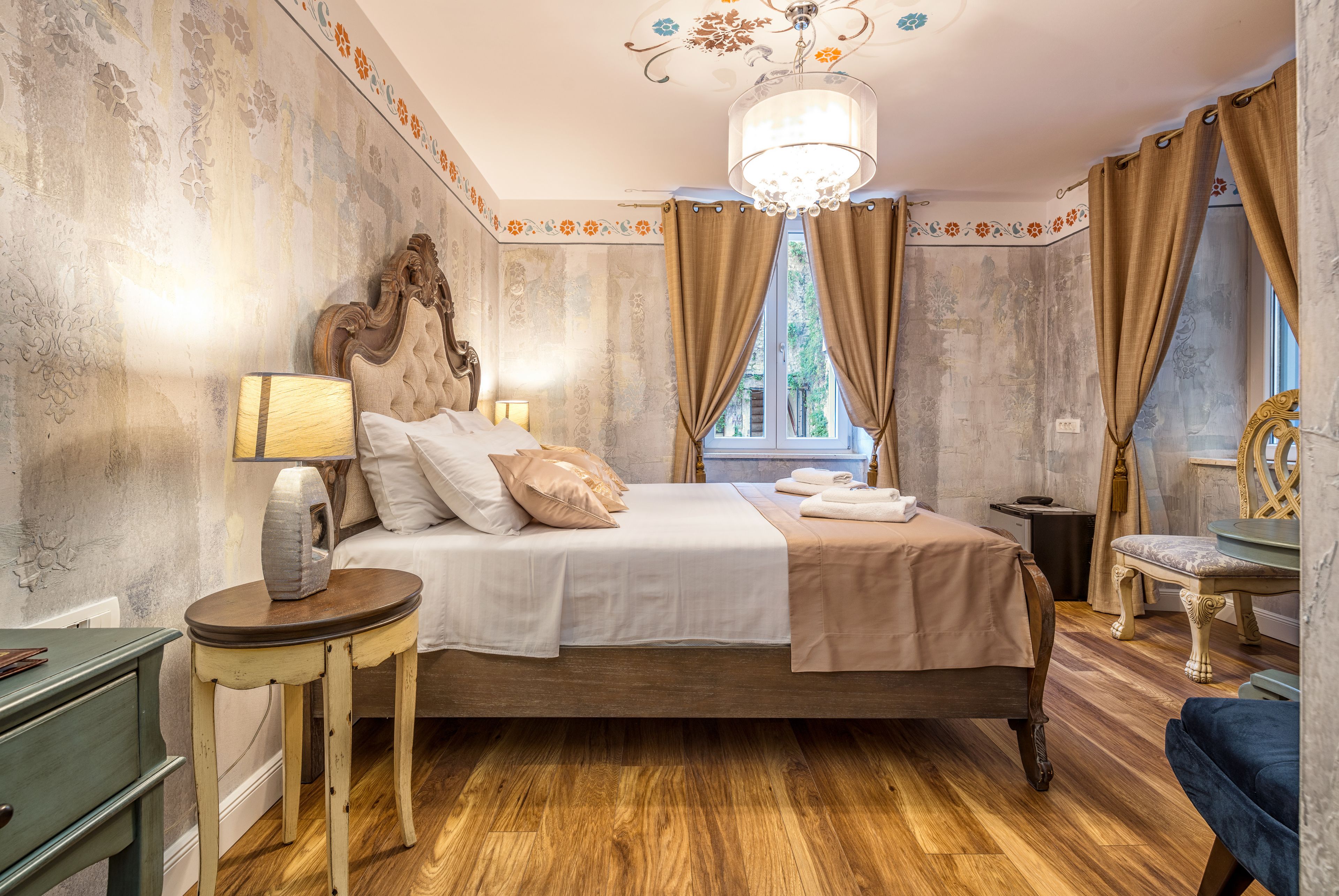A bedroom with a large bed, a bedside table, a chair, and a window with curtains.