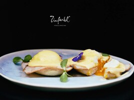 Ein Teller mit einem Gericht, das wie ein pochiertes Ei mit Sauce Hollandaise wirkt, garniert mit einer kleinen violetten Blume und grünen Blättern.