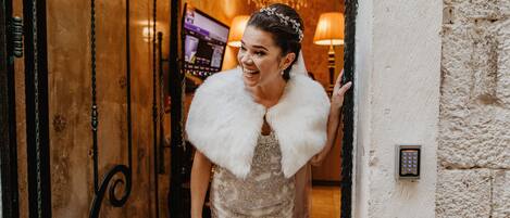 A woman in a white dress with a fur collar entering a room with a chandelier and a wall-mounted light switch.