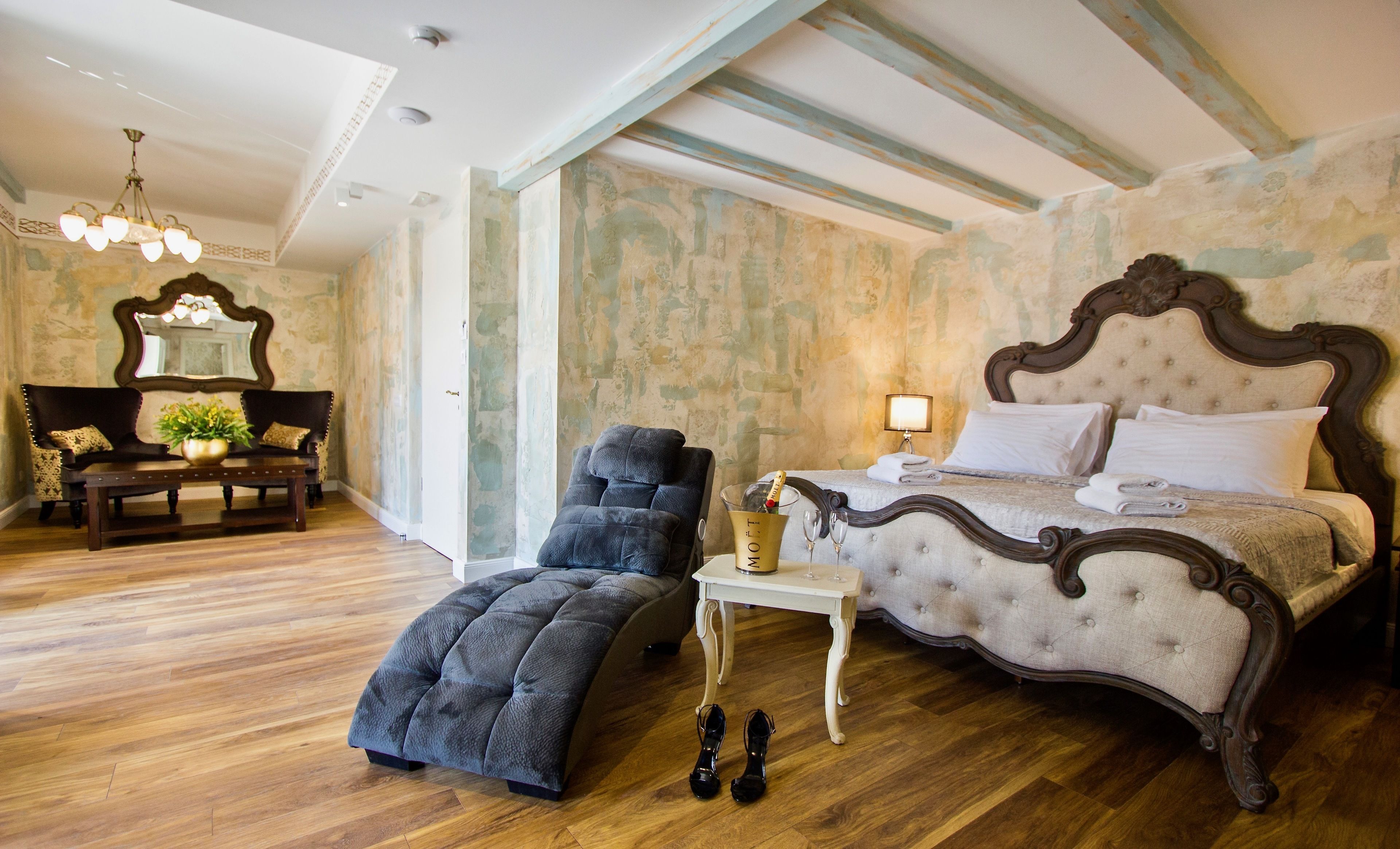 Un dormitorio con una cama grande, un chaise lounge, una mesita con una botella de champán y un espejo.
