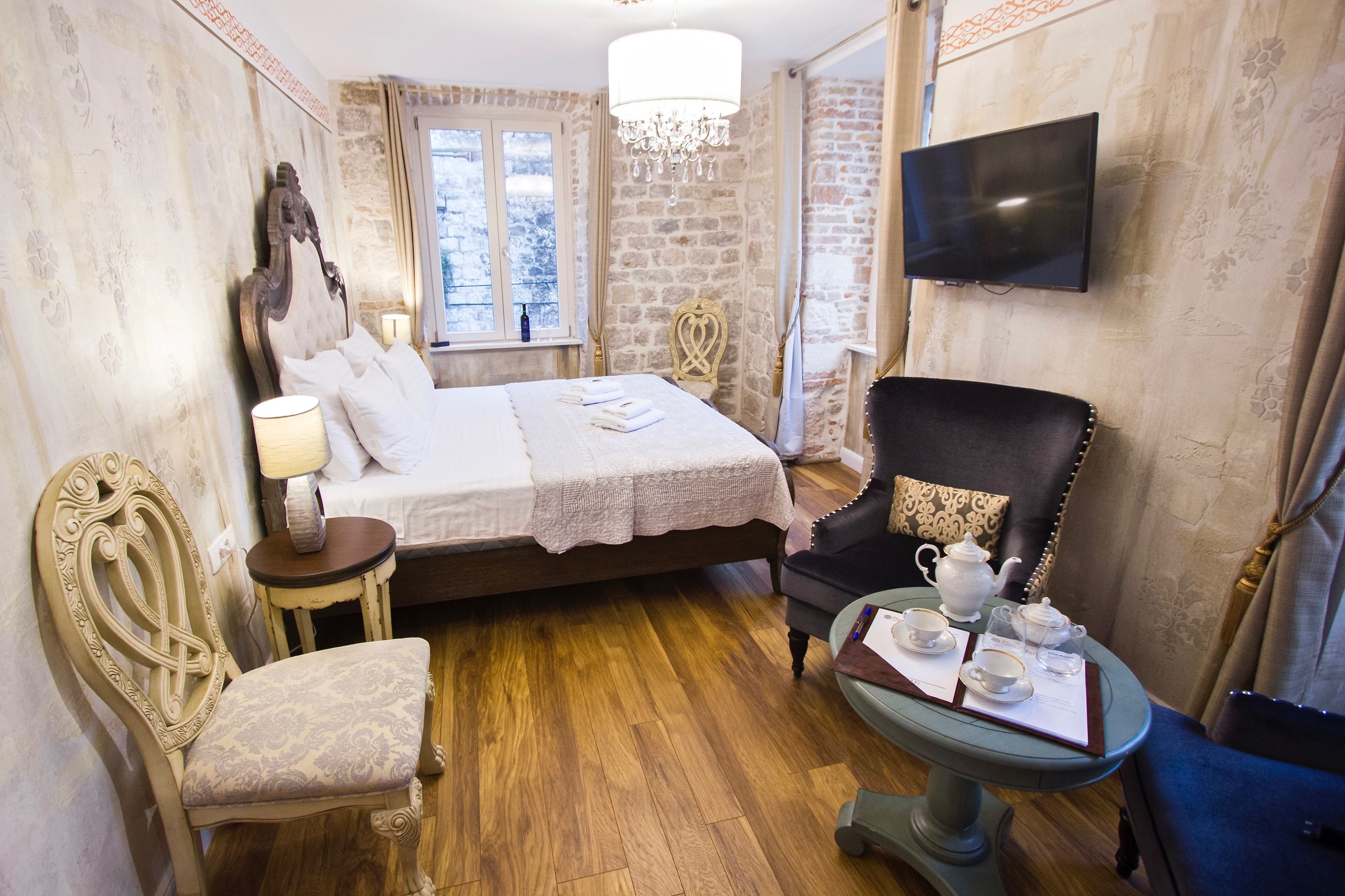 Habitación de hotel con una cama grande, una silla, una mesita con juego de té, un televisor y una ventana con vistas a árboles.