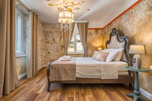A bedroom with a stone wall, a wooden bed, a chandelier, and a window with curtains.
