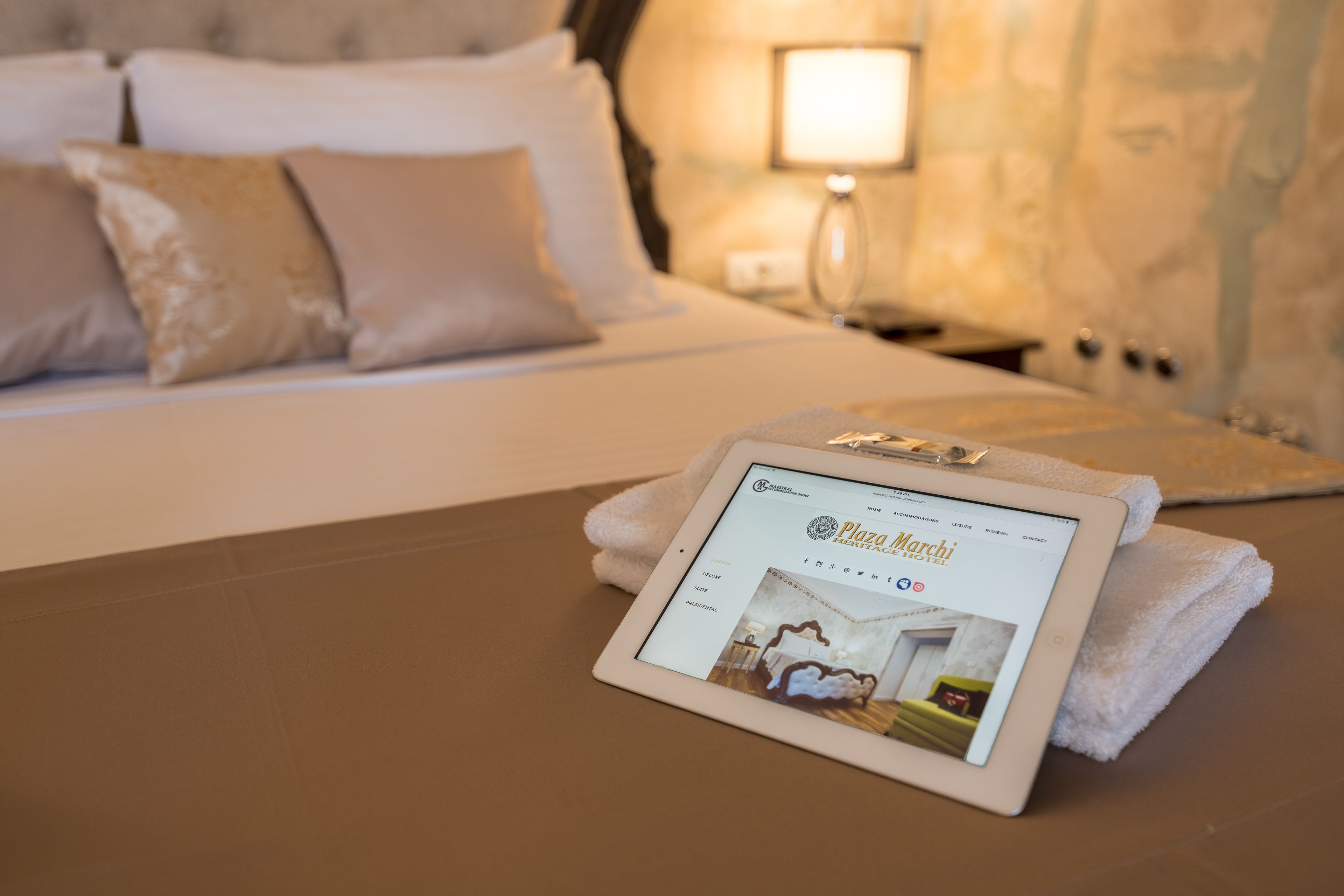 A tablet displaying a hotel website on a bed with a neatly folded white towel.