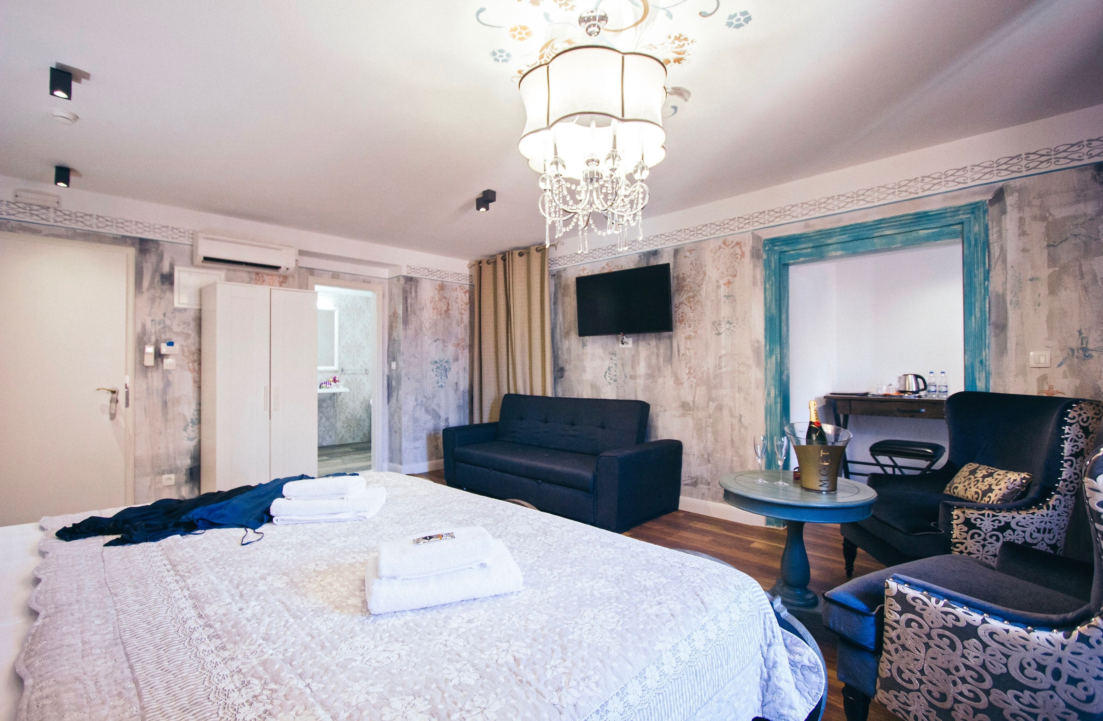 Quarto de hotel com uma cama grande, um sofá, uma pequena mesa com uma garrafa e uma televisão na parede.