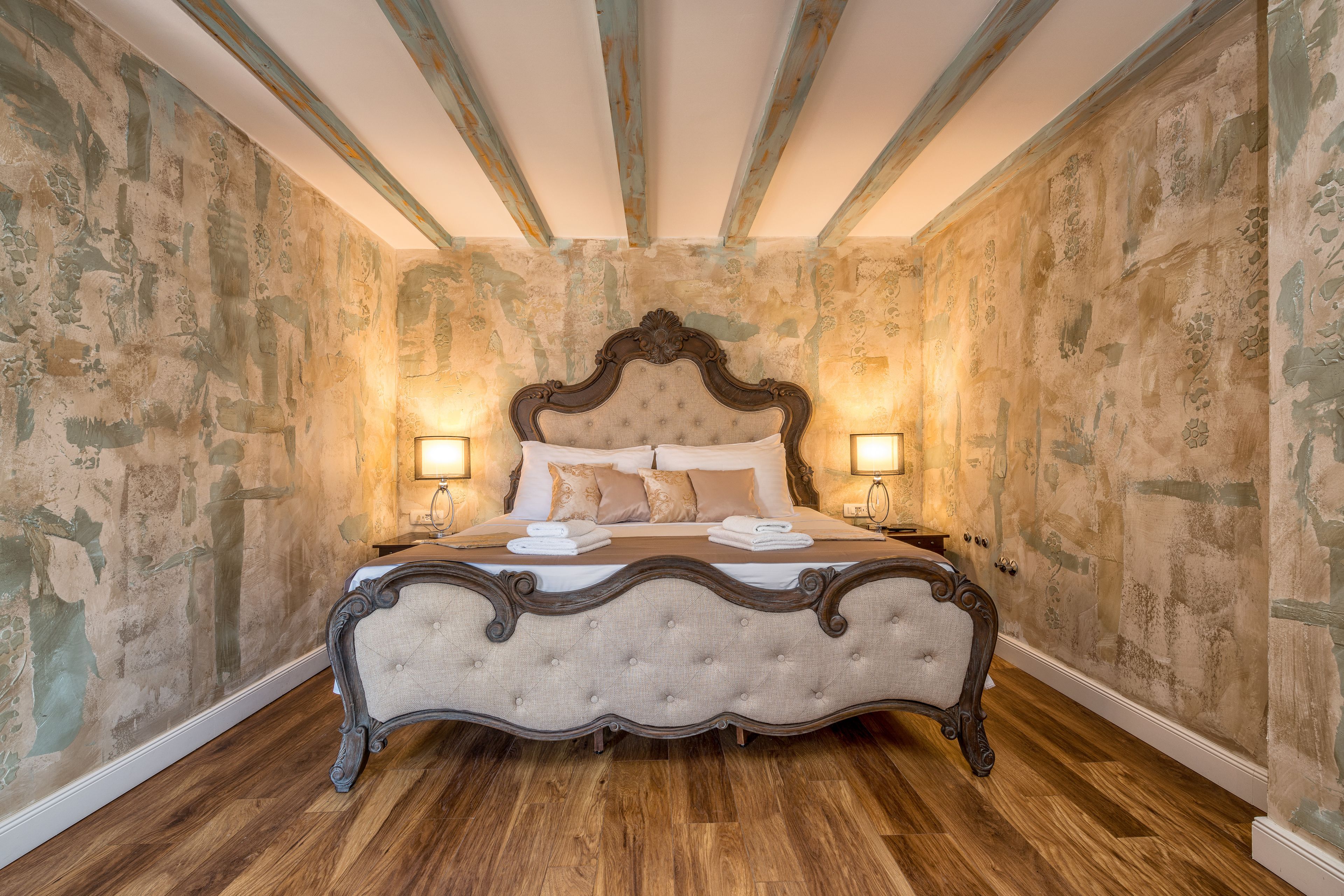 A bedroom with a large bed, wooden floor, and a ceiling with exposed beams.