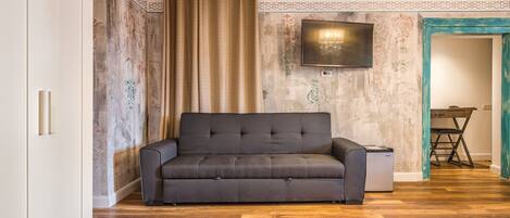 A modern living room with a grey sofa, a flat-screen TV mounted on the wall, and a wooden floor.