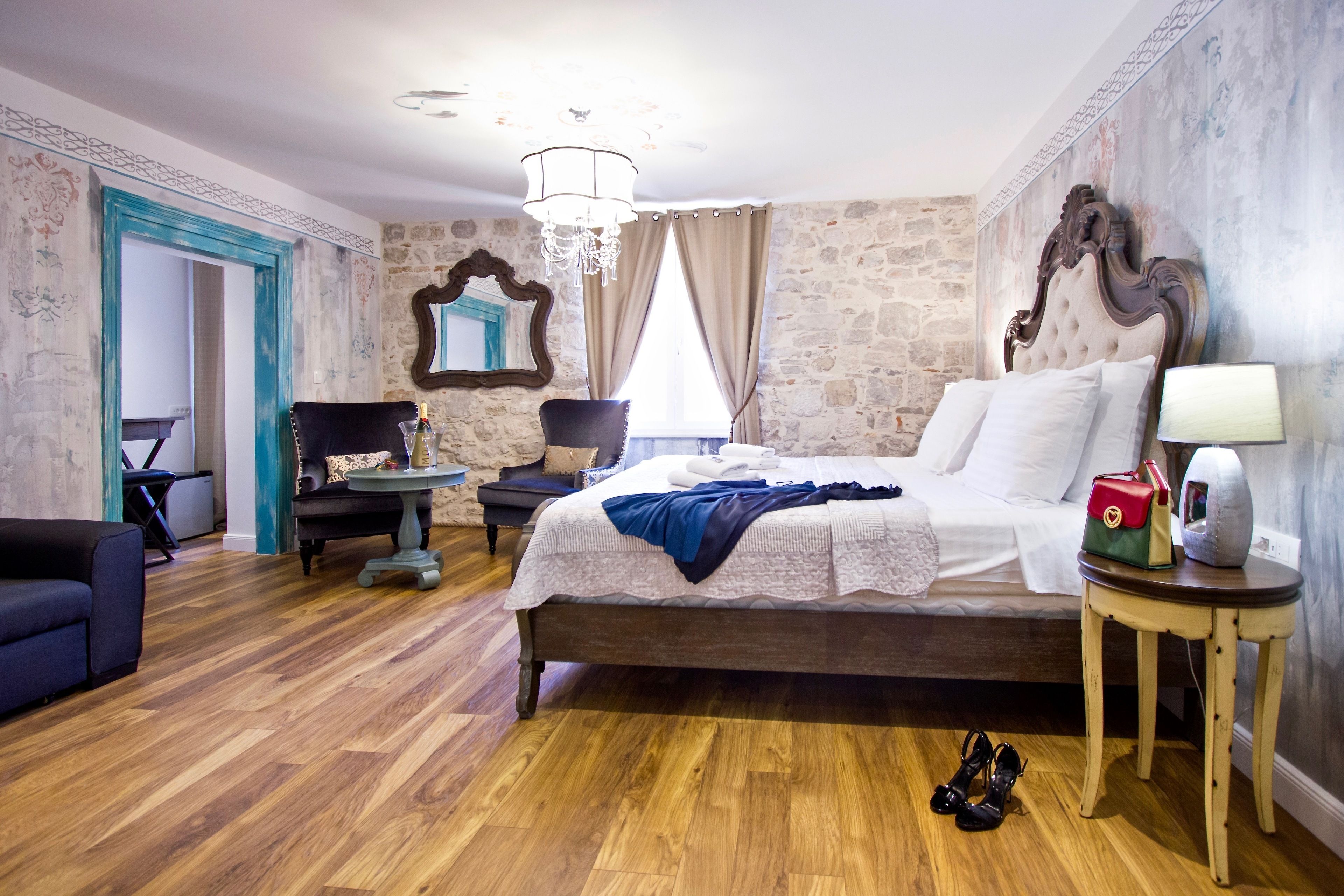 A bedroom with a large bed, a chair, a small table, and a mirror on the wall.