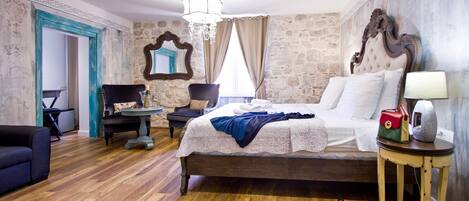 A bedroom with a large bed, a chair, a small table, and a mirror on the wall.