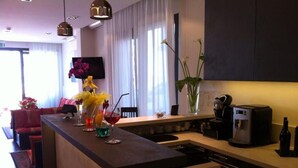 A modern kitchen with a central island, a flat-screen TV mounted on the wall, and a dining area with a red sofa. - Hotel Aurora (Gabicce Mare)