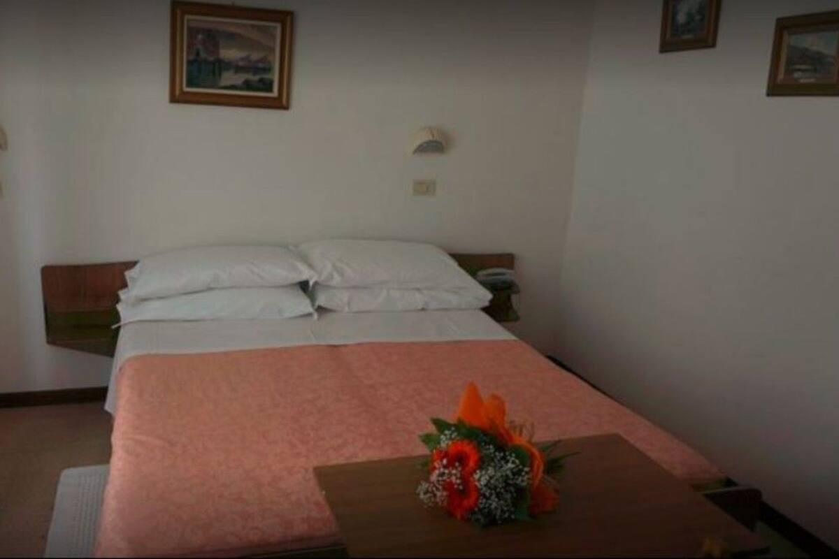 A hotel room with a bed, a nightstand, a small table with a flower arrangement, and two wall-mounted lamps.