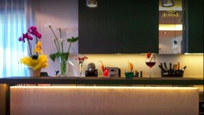 A bar area with a counter, various bottles, a wine glass, and a vase with flowers. - Hotel Aurora (Gabicce Mare)