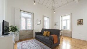 A modern living room with a grey sofa, a wooden floor, and a large window providing natural light. - Apartment Alegria Street by Sweet Porto - Free Parking (Porto)