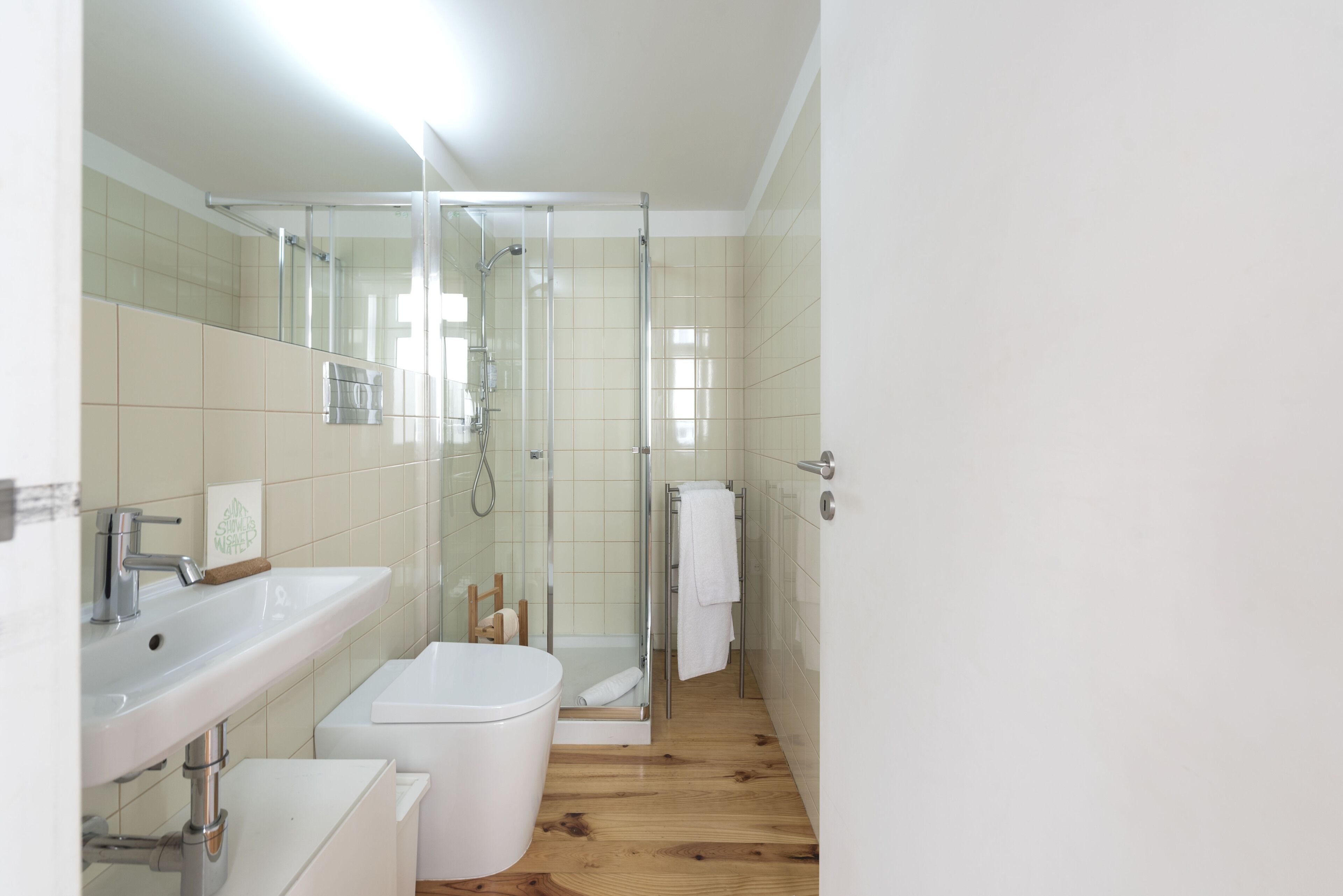 A modern bathroom with a glass shower enclosure, a white sink, and a wooden floor.