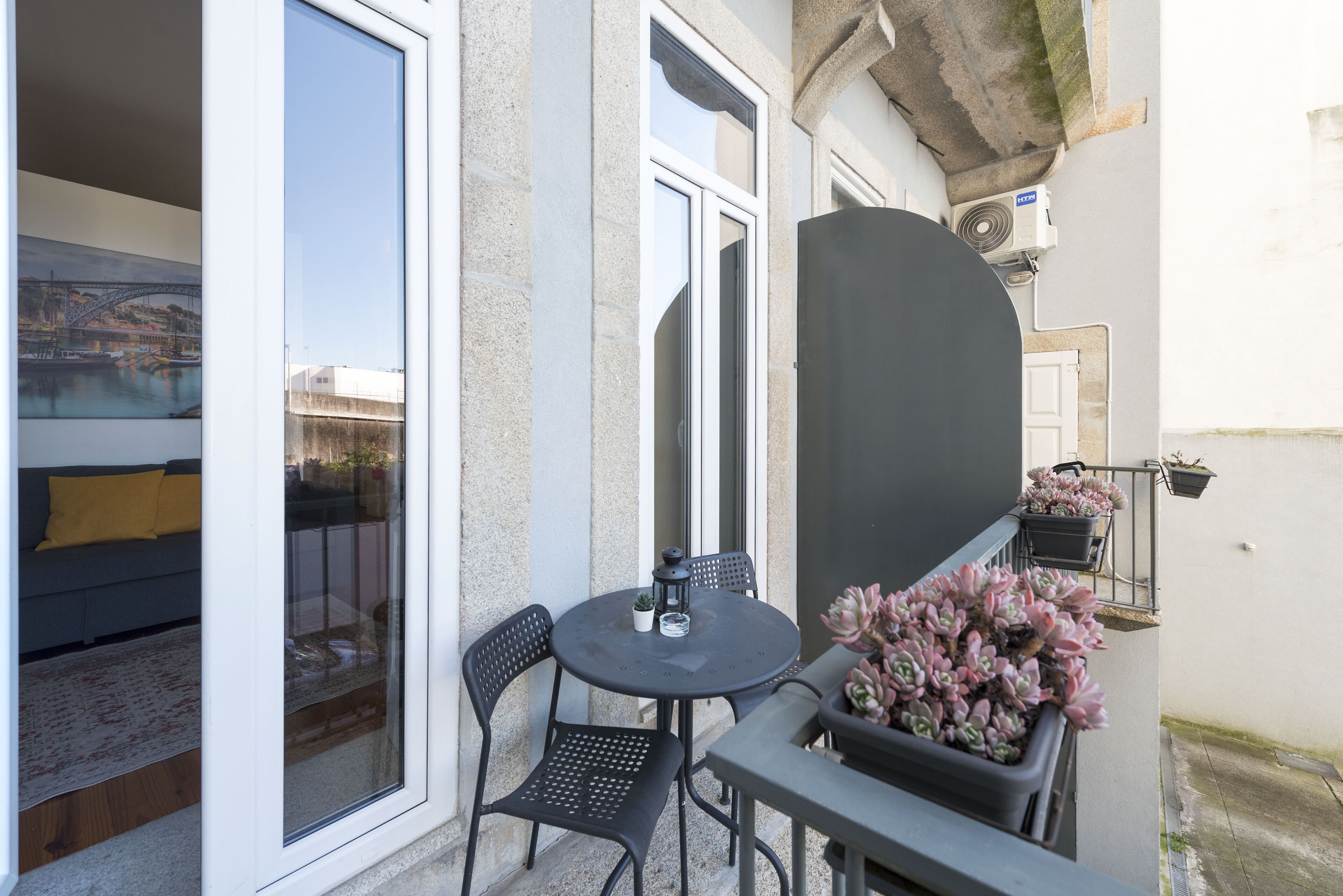 A balcony with a table and chairs, a potted plant, and a view of a building through a glass door.