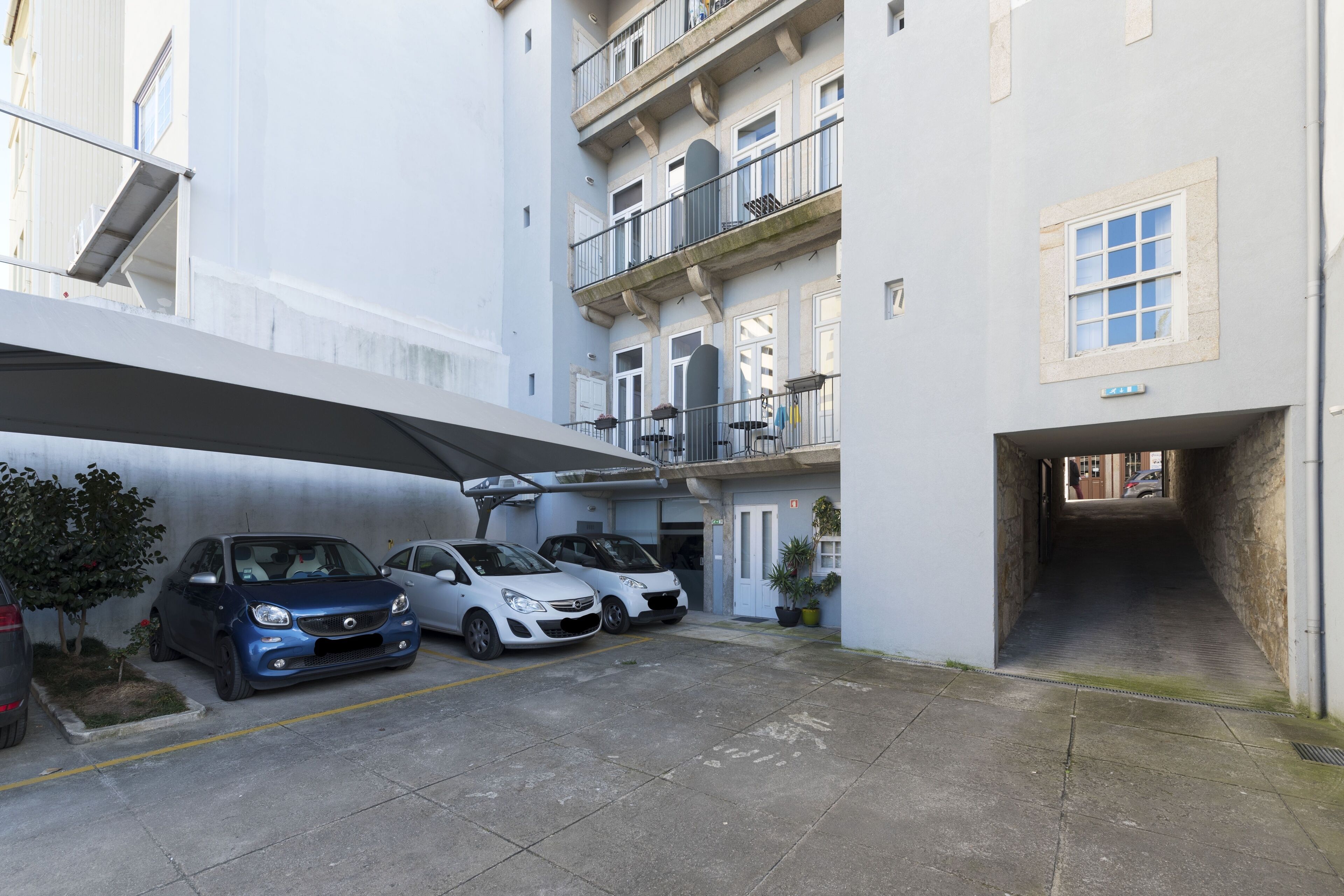 Un’area di parcheggio con tre auto, una tettoia e un edificio con balconi e finestre.