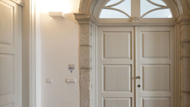 A white door with a stone archway, a light switch, and a thermostat on the wall. - Apartment Alegria Street by Sweet Porto - Free Parking (Porto)