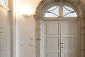 A white door with a stone archway, a light switch, and a thermostat on the wall.