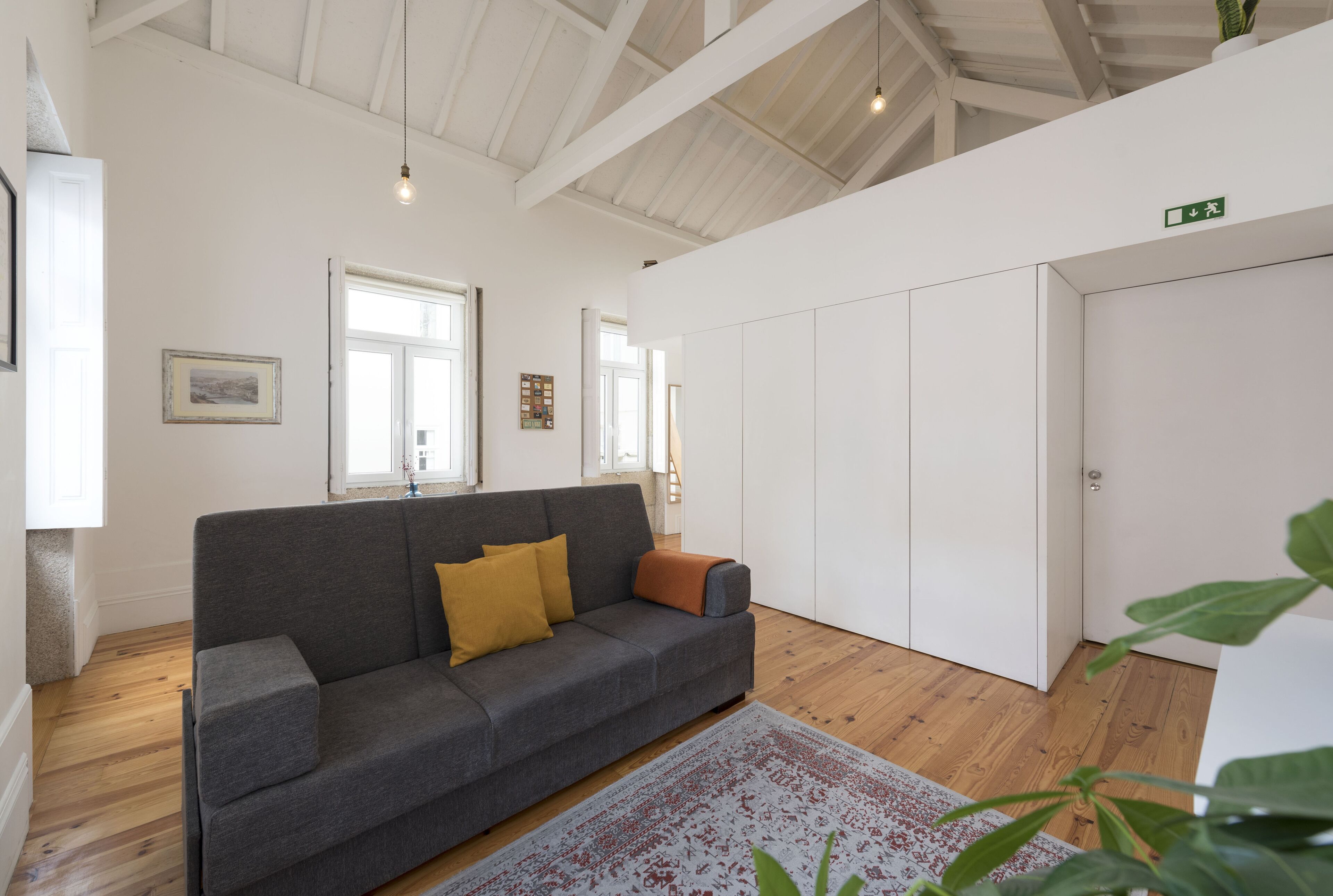 A modern living room with a grey sofa, a patterned rug, wooden flooring, and white walls.
