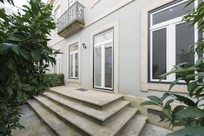 A building with a stone staircase leading to a door, surrounded by greenery.