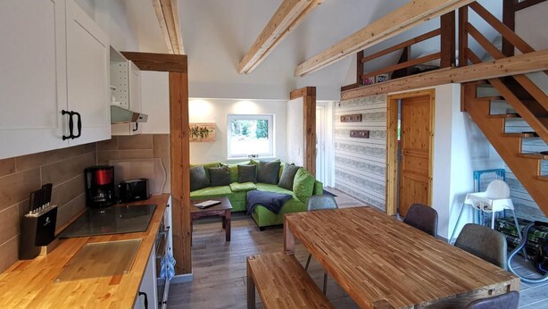 A modern kitchen with wooden cabinets, a coffee machine, and a dining area with a wooden table and benches. - Naturhof Usedom (Mölschow)