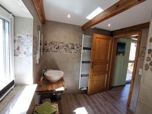 Une salle de bain avec un mur recouvert d’une mosaïque de pierre, un meuble-lavabo en bois, un grand lavabo blanc et une porte en bois.