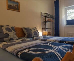Une chambre avec deux lits, une étagère en métal, un tableau encadré accroché au mur et une fenêtre avec des rideaux.