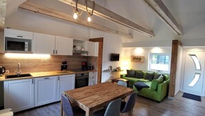 A modern kitchen with white cabinets, a wooden dining table, and a green sofa in the living area. - Naturhof Usedom (Mölschow)
