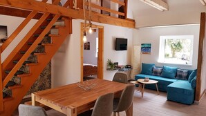 A cozy living room with a wooden staircase, a dining area with a wooden table, and a blue sofa. - Naturhof Usedom (Mölschow)