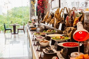 A buffet setup with various food items and a red lamp. - Aria Grand Hotel & Spa (Da Nang)