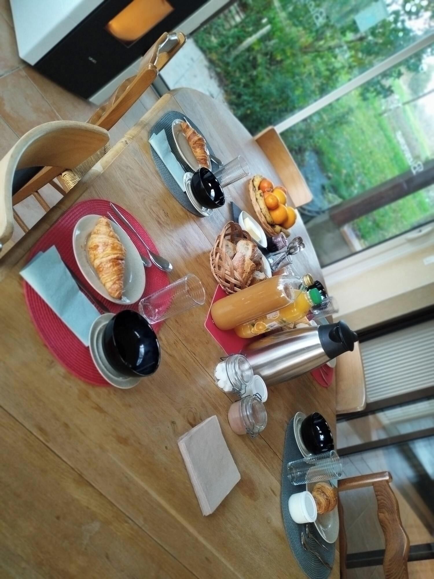 Desayuno con cruasanes, pan, frutas y salsas sobre una mesa de madera.