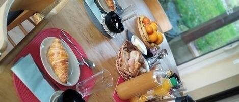 Desayuno con cruasanes, pan, frutas y salsas sobre una mesa de madera.