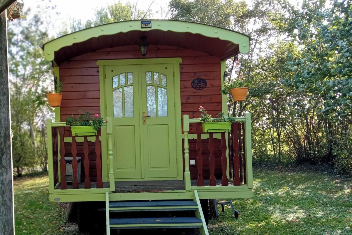 Une petite cabane en bois d’un seul étage, avec une porte et des fenêtres vertes, un petit porche doté d’une balustrade et une marche menant à l’entrée.
