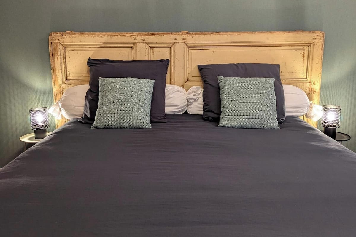 Un lit recouvert d’une couvre-lit de couleur sombre, agrémenté de deux coussins à motifs, et flanqu é de deux lampes de chevet.