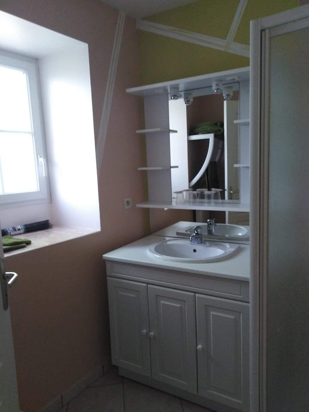 A bathroom with a window, a sink, a mirror, and a cabinet.