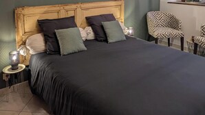 Une chambre à coucher avec un grand lit, une tête de lit en bois, une table de chevet avec une lampe, une chaise et une fenêtre donnant sur des arbres.