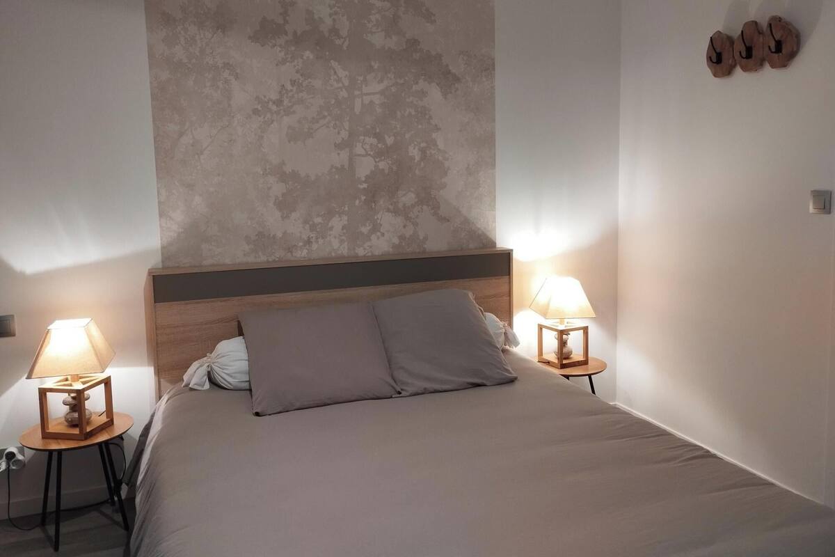Une chambre à coucher avec un lit, deux tables de chevet avec des lampes, une tête de lit et un mur orné d’une fresque représentant un arbre.
