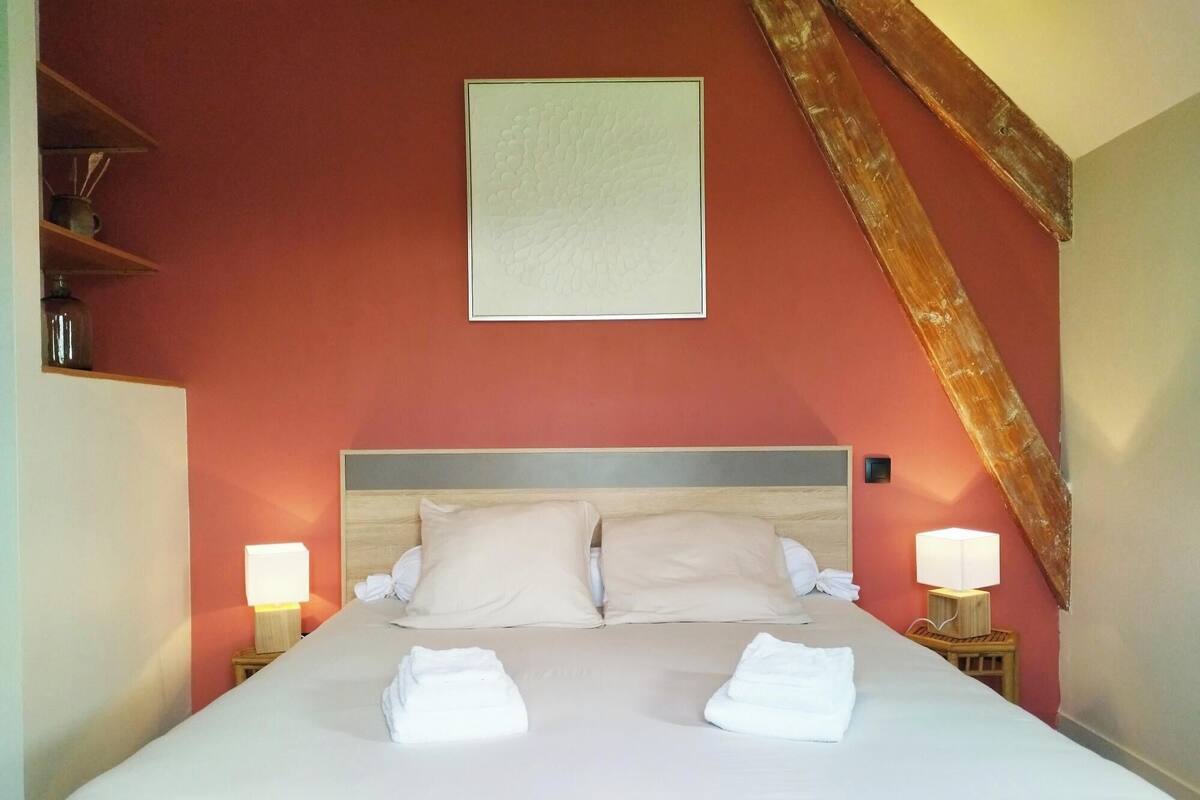 Un lit bien fait, avec deux serviettes pliées, une tête de lit en bois et deux lampes de chevet.