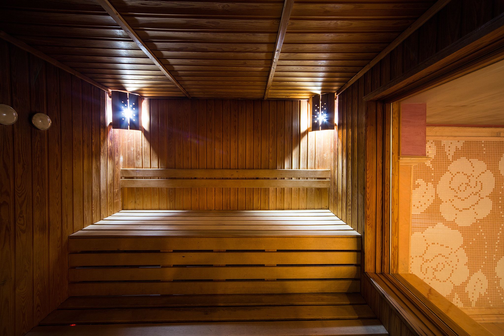 Uma sauna de madeira com bancos e parede revestida de azulejos.