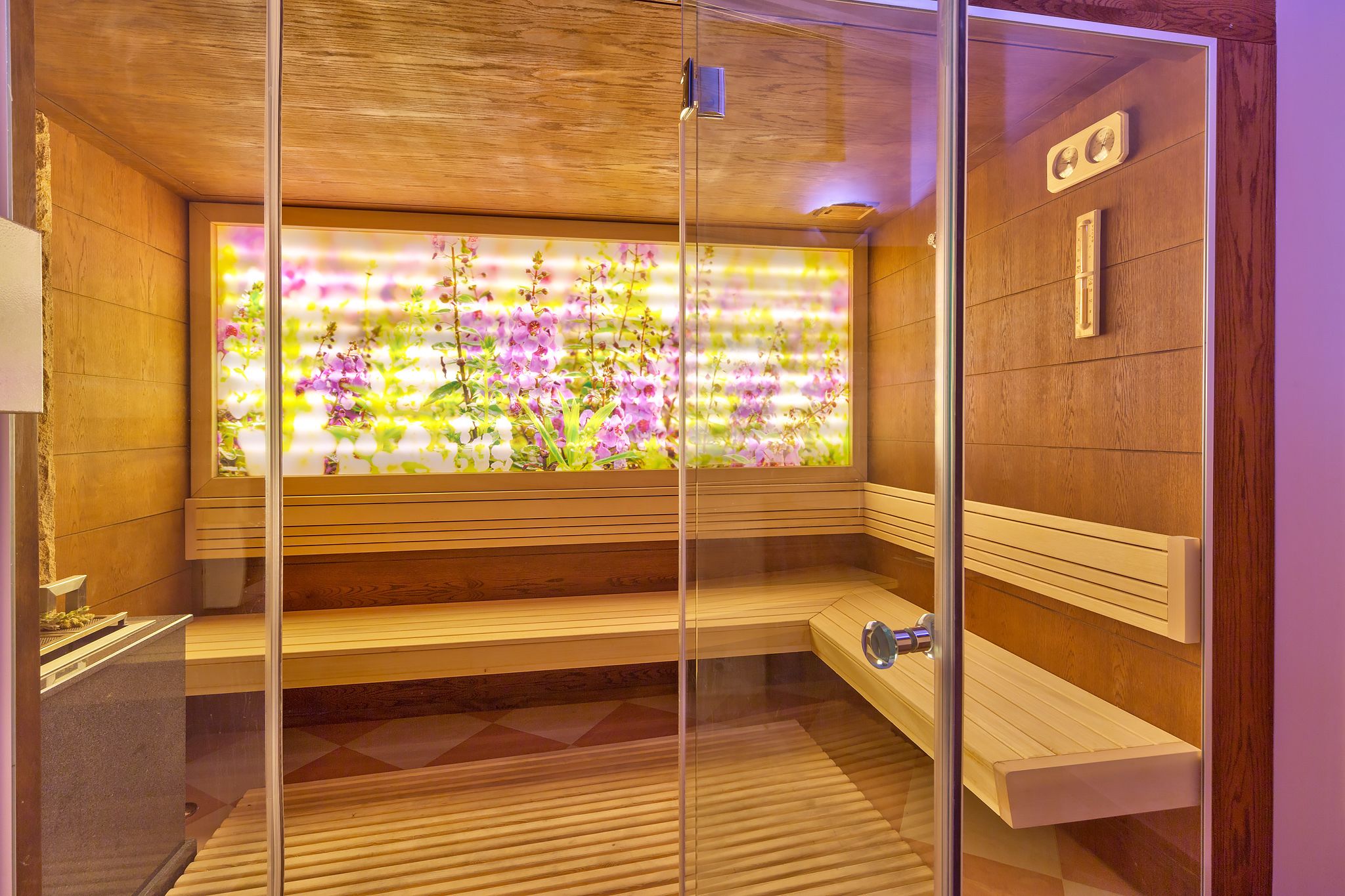 Una sauna con bancos de madera y un muro de cristal que muestra flores de colores.